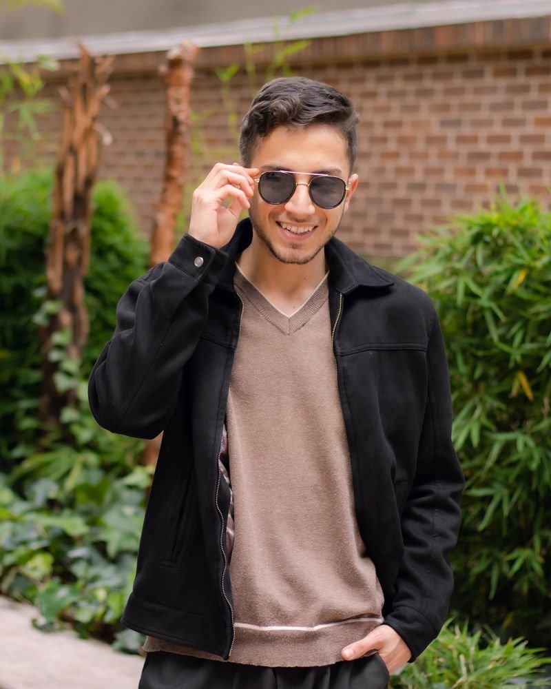 Lucas Agudelo Muñoz sonriente, con chaqueta negra y gafas de sol, en un jardín